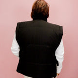 Person wearing a black vest over a white shirt on a pink background