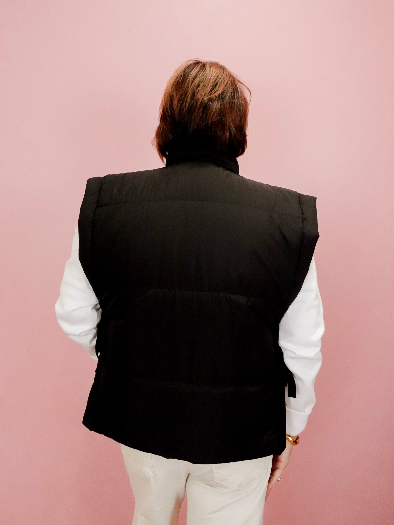 Person wearing a black vest over a white shirt on a pink background