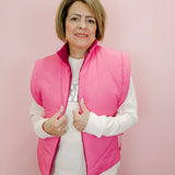 Woman wearing a pink puffer vest over a white shirt on a pink background