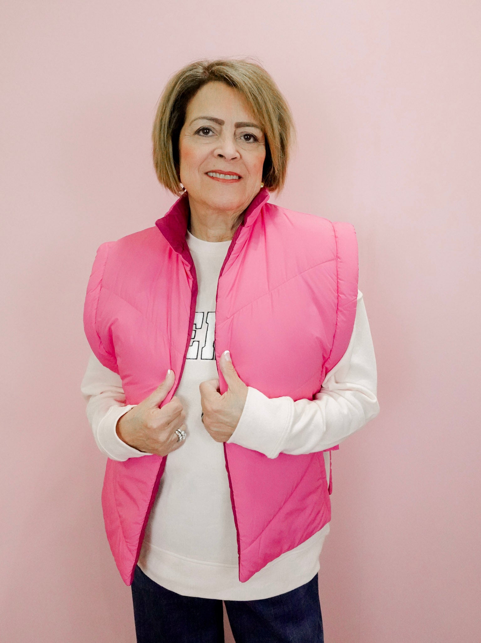 Woman wearing a pink puffer vest over a white shirt on a pink background