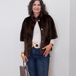 Woman wearing a brown fur coat, white shirt, blue jeans, and gold belt against a white wall.