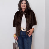 Woman wearing a brown fur coat, white shirt, blue jeans, and gold belt against a white wall.