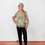 Person wearing a patterned shirt and black pants against a white wall.