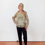Person wearing a patterned shirt and black pants against a white wall.
