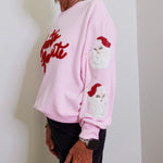 Person wearing a pink sweatshirt with Santa Claus design and text.