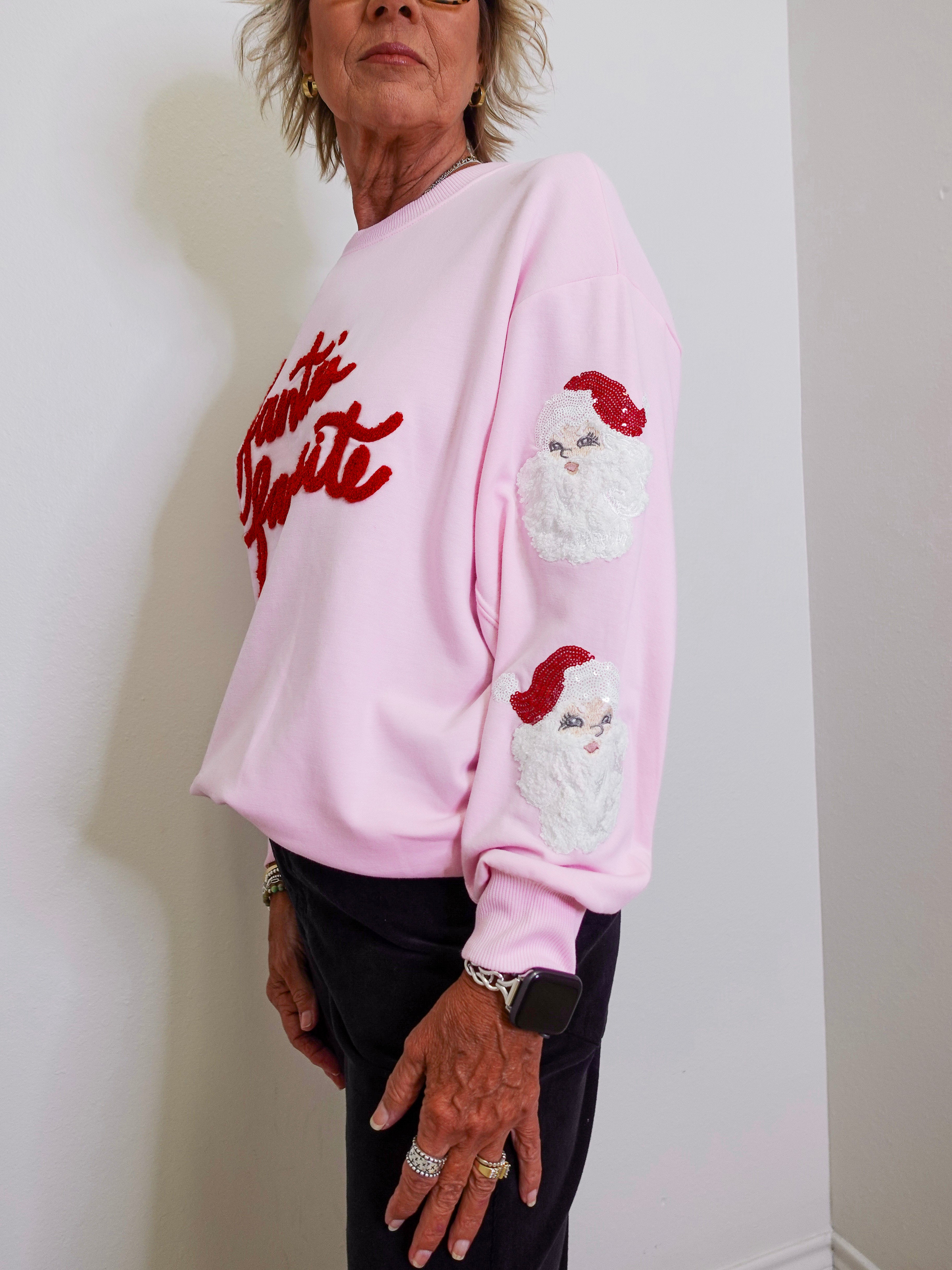 Person wearing a pink sweatshirt with Santa Claus design and text.