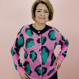 Woman wearing a pink cardigan with green leopard print pattern against a pink background