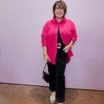 Woman wearing a pink shirt and black pants against a light purple wall.