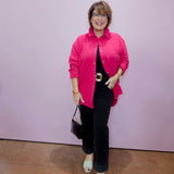 Woman wearing a pink shirt and black pants against a light purple wall.