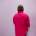 Person wearing a pink quilted jacket against a light purple background