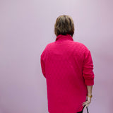 Person wearing a pink quilted jacket against a light purple background