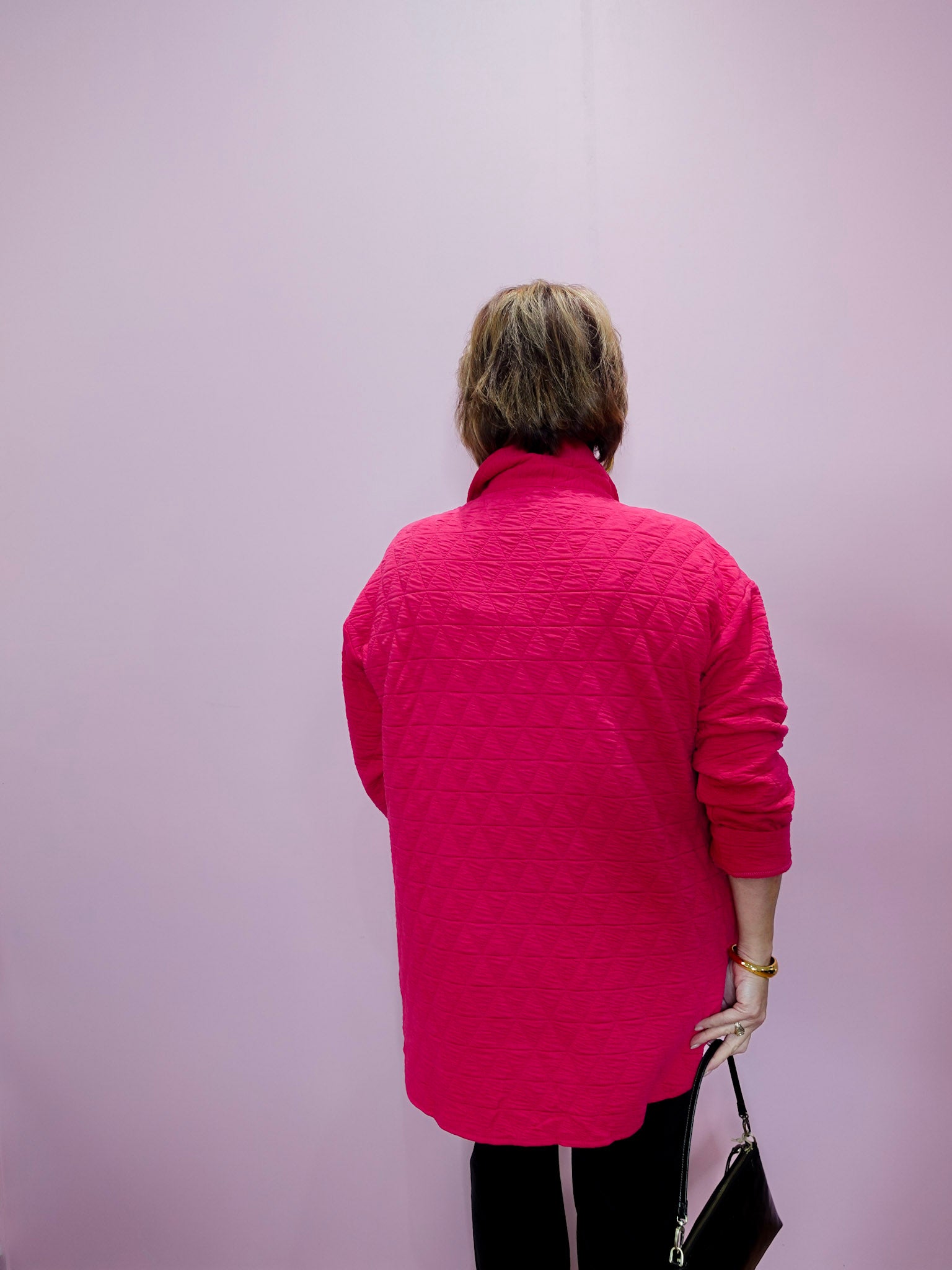 Person wearing a pink quilted jacket against a light purple background