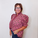 Woman wearing a pink patterned blouse and blue jeans against a white background