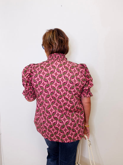 Person wearing a pink patterned blouse against a white wall