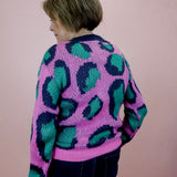 Person wearing a pink sweater with green and blue leopard print pattern against a plain background