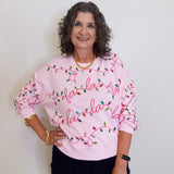 Woman wearing a pink sweatshirt with 'fa la la' text and Christmas lights design against a plain background