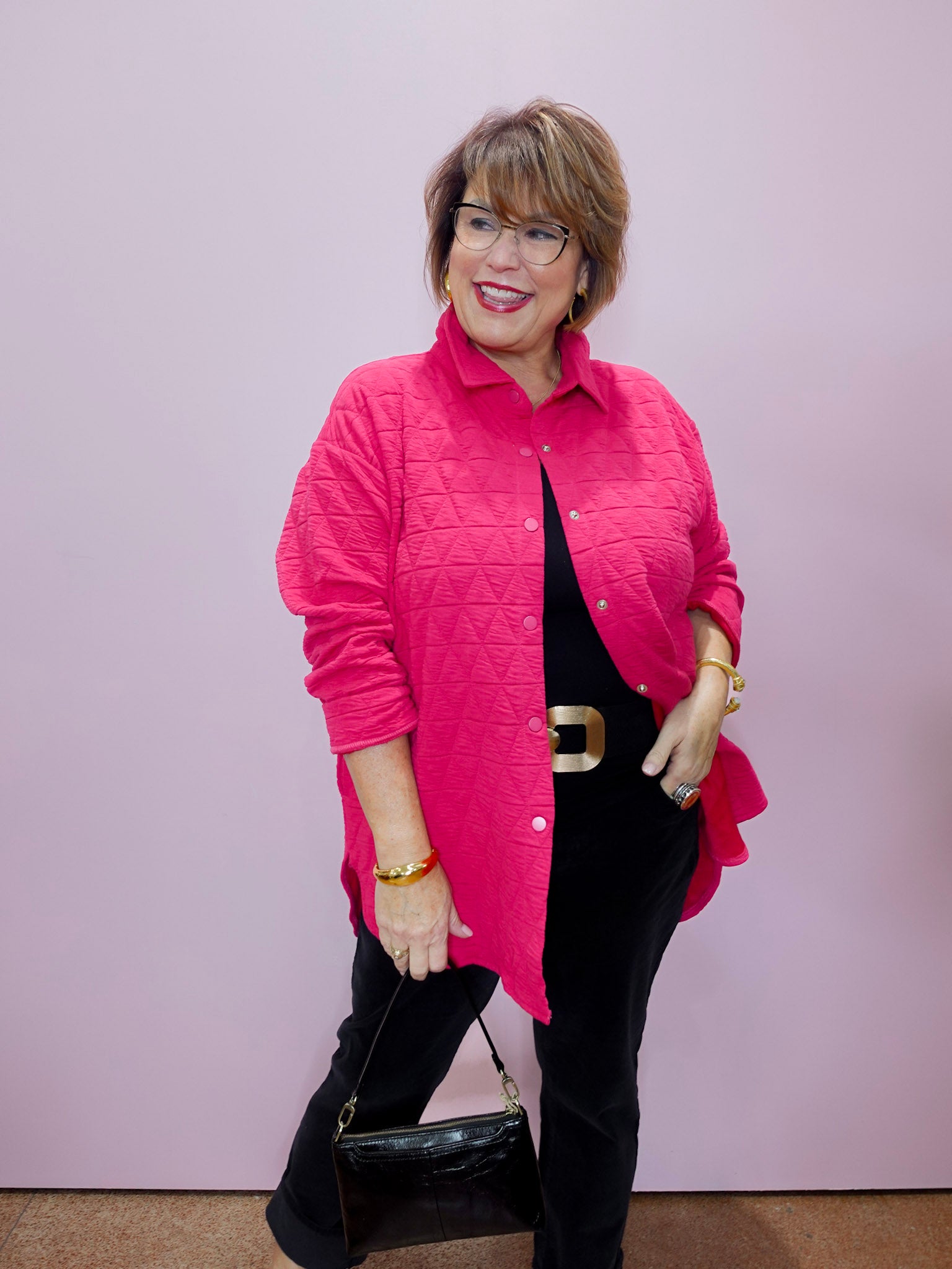 Woman wearing a pink quilted jacket and black pants against a plain background