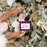 Person holding a photo frame ornament in front of a decorated Christmas tree.