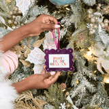 Person holding a photo frame ornament in front of a decorated Christmas tree.