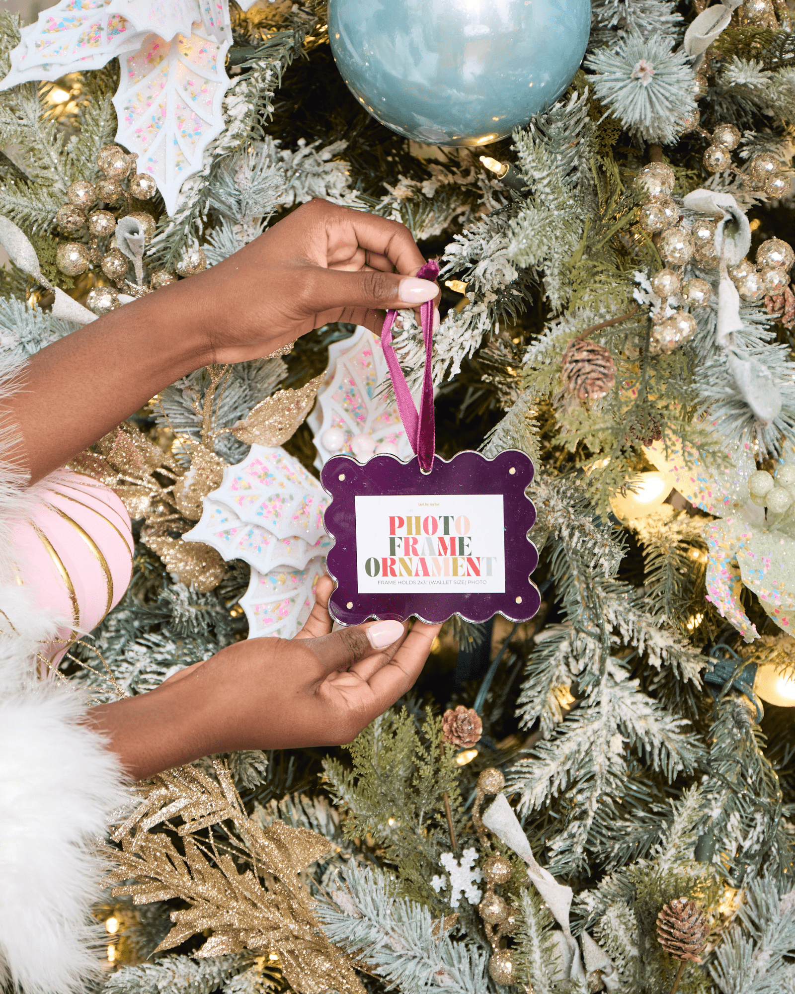 Person holding a photo frame ornament in front of a decorated Christmas tree.