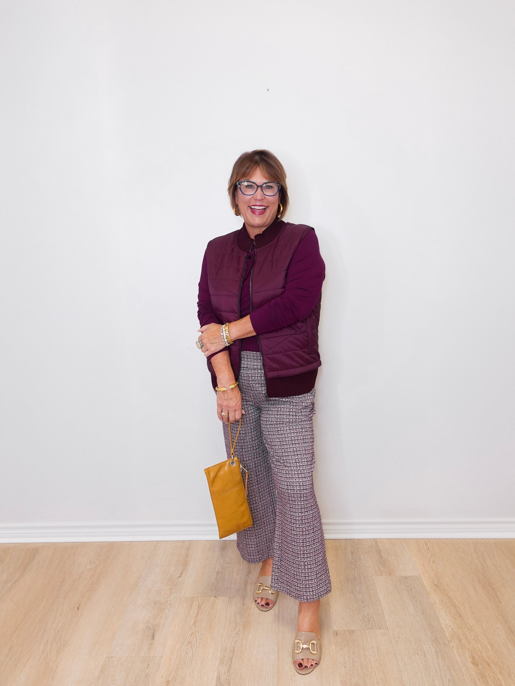 Woman wearing a purple jacket and plaid pants standing against a white wall.