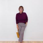 Woman wearing a purple sweater and patterned pants against a white wall.