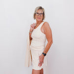 Woman wearing a white dress and beige cardigan against a white background