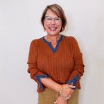 Woman wearing a rust sweater with blue trim against a white background
