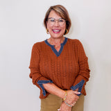 Woman wearing a rust sweater with blue trim against a white background