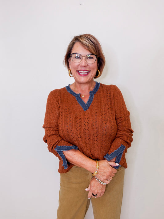 Woman wearing a rust sweater with blue trim against a white background