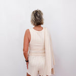 Person wearing a white dress with a beige cardigan against a plain background