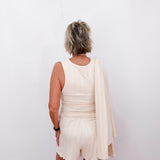 Person wearing a white dress with a beige cardigan against a plain background