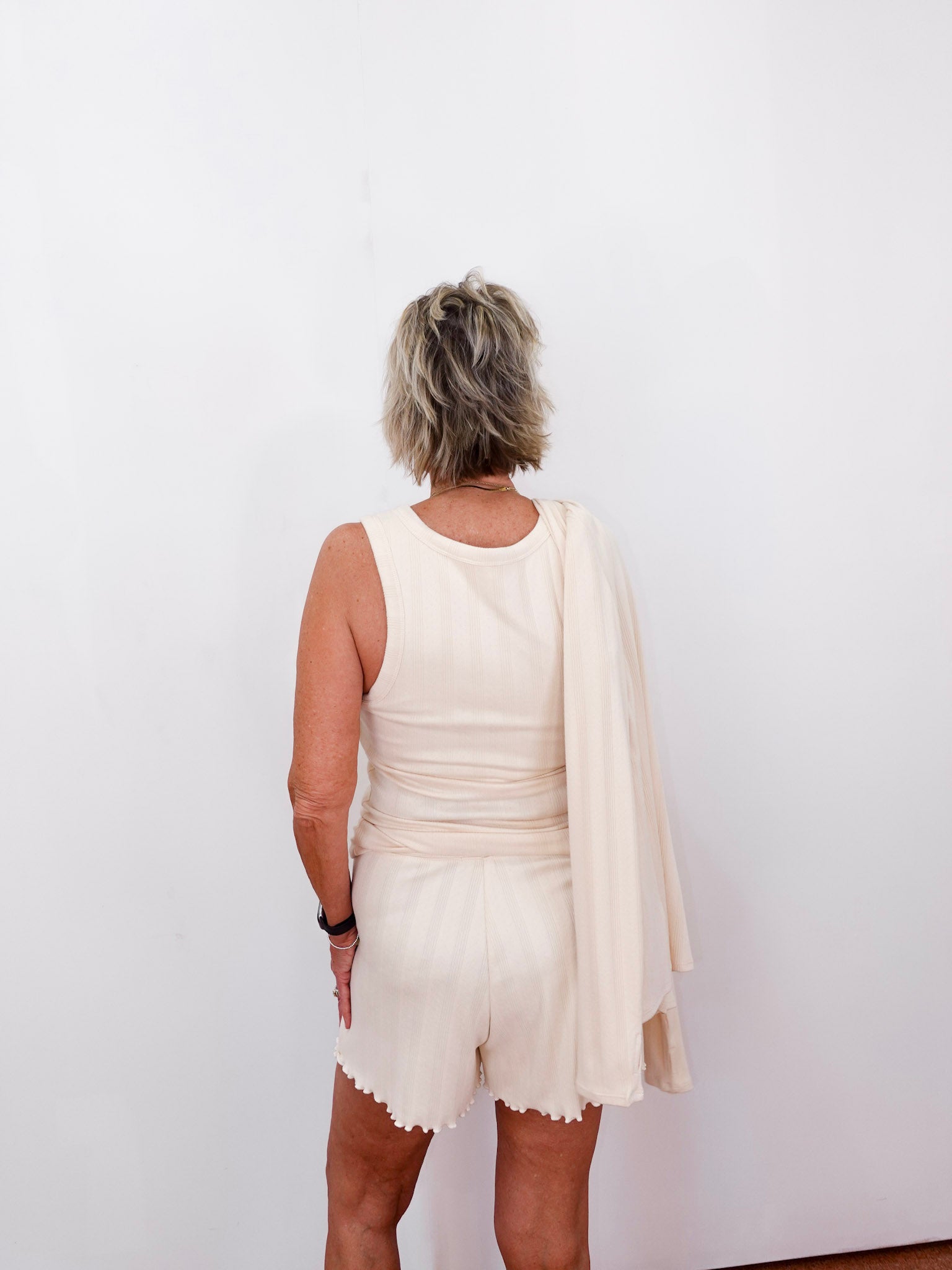 Person wearing a white dress with a beige cardigan against a plain background