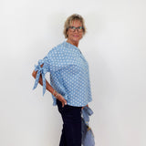 Woman wearing a blue polka dot top and dark pants against a white wall.
