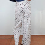 White wide-leg trousers with a black polka dot pattern, shown on a model from the back wearing a blue denim shirt and brown sandals.