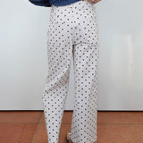 White wide-leg trousers with a black polka dot pattern, shown on a model from the back wearing a blue denim shirt and brown sandals.