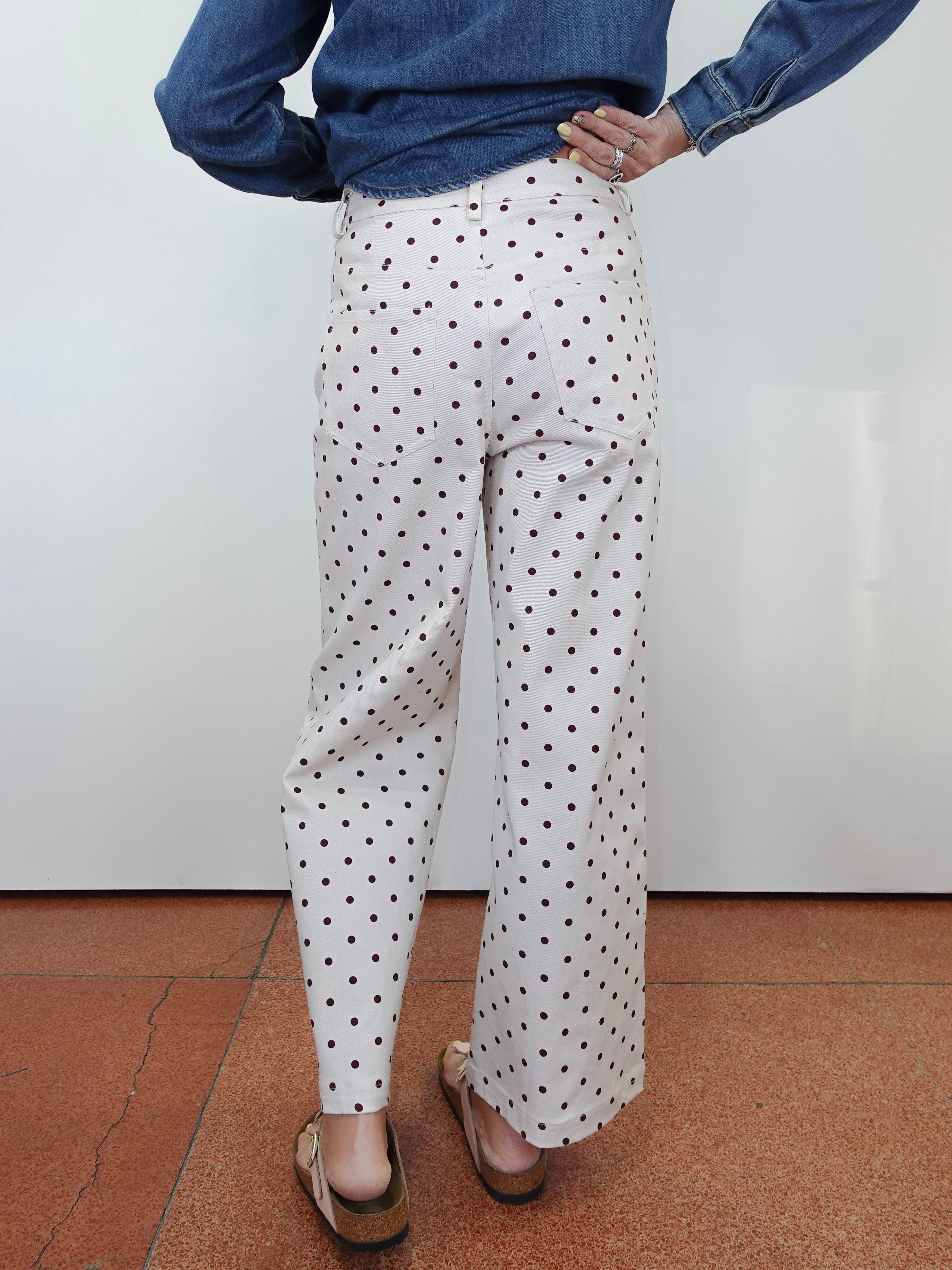 White wide-leg trousers with a black polka dot pattern, shown on a model from the back wearing a blue denim shirt and brown sandals.
