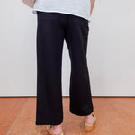 Person wearing black wide-leg pants and a light-colored top on a plain background