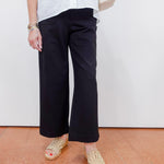 Person wearing black pants and white top with beige shoes on a plain background