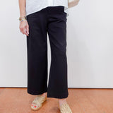 Person wearing black pants and white top with beige shoes on a plain background