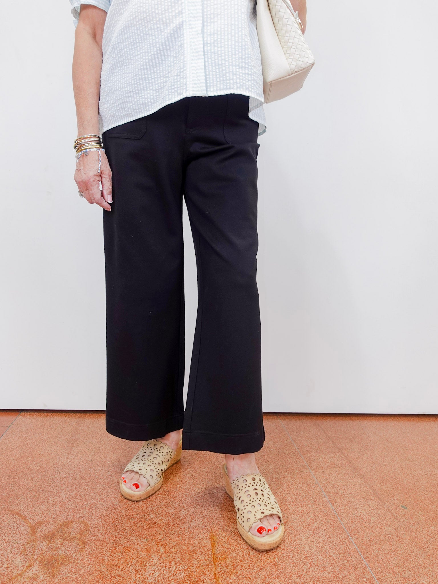 Person wearing black pants and white top with beige shoes on a plain background