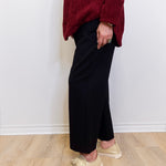 Woman wearing a black wide leg pant against a white background. 