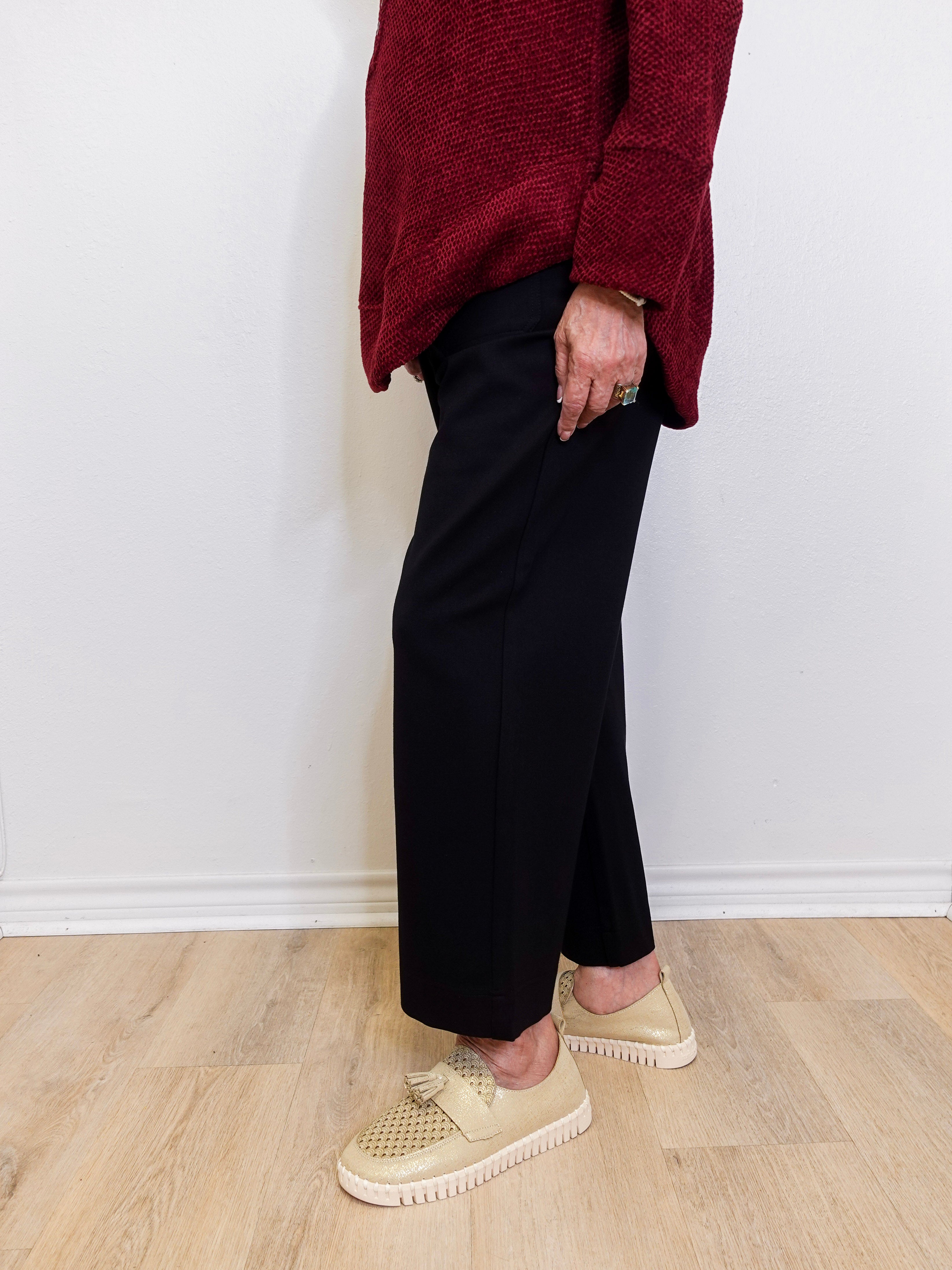 Woman wearing a black wide leg pant against a white background. 