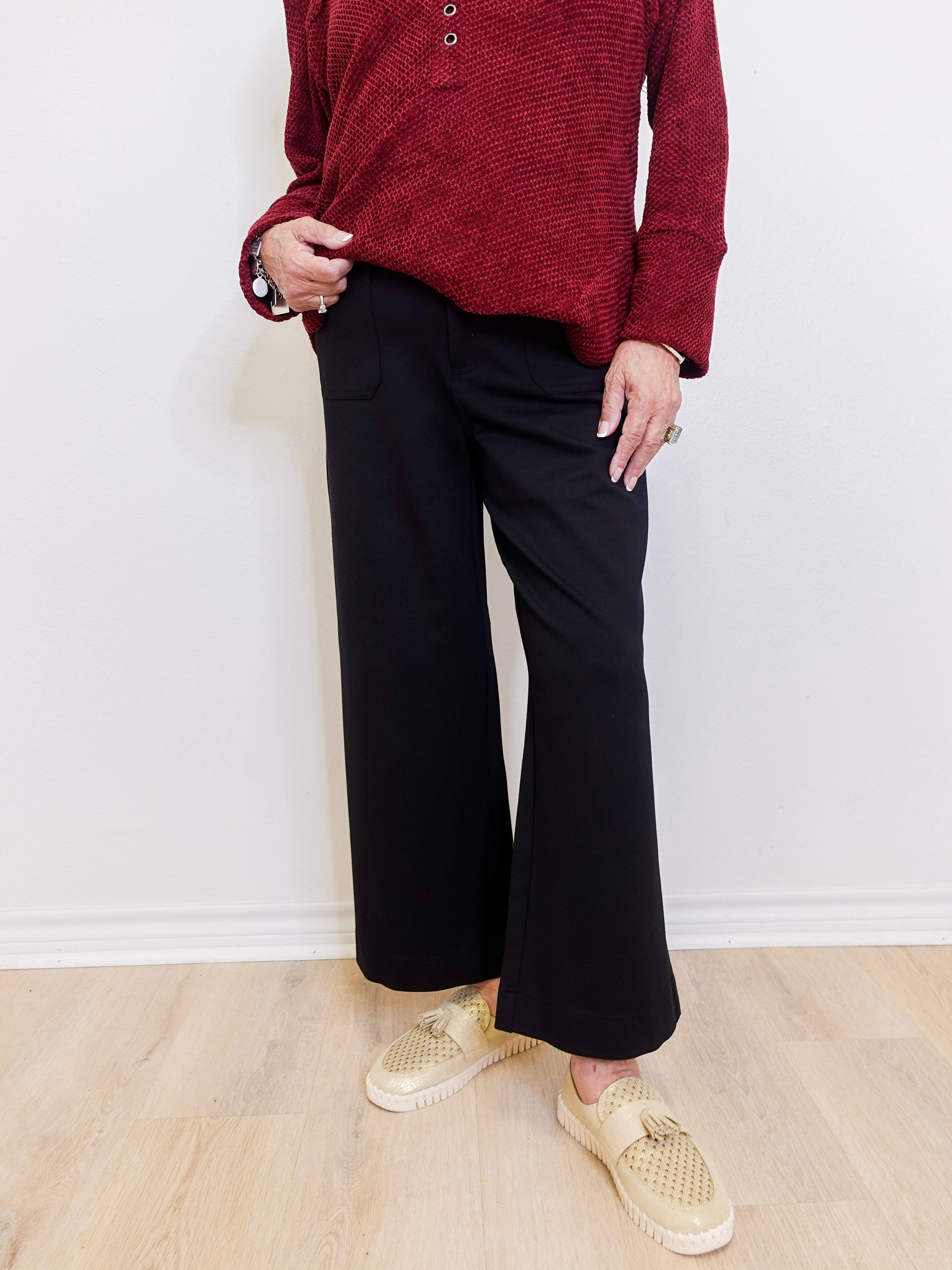 Woman wearing a black cropped wide leg pant against a white background. 