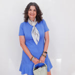 Woman in a blue dress with a white scarf and handbag against a white background