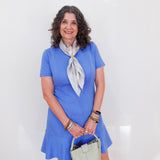 Woman in a blue dress with a white scarf and handbag against a white background