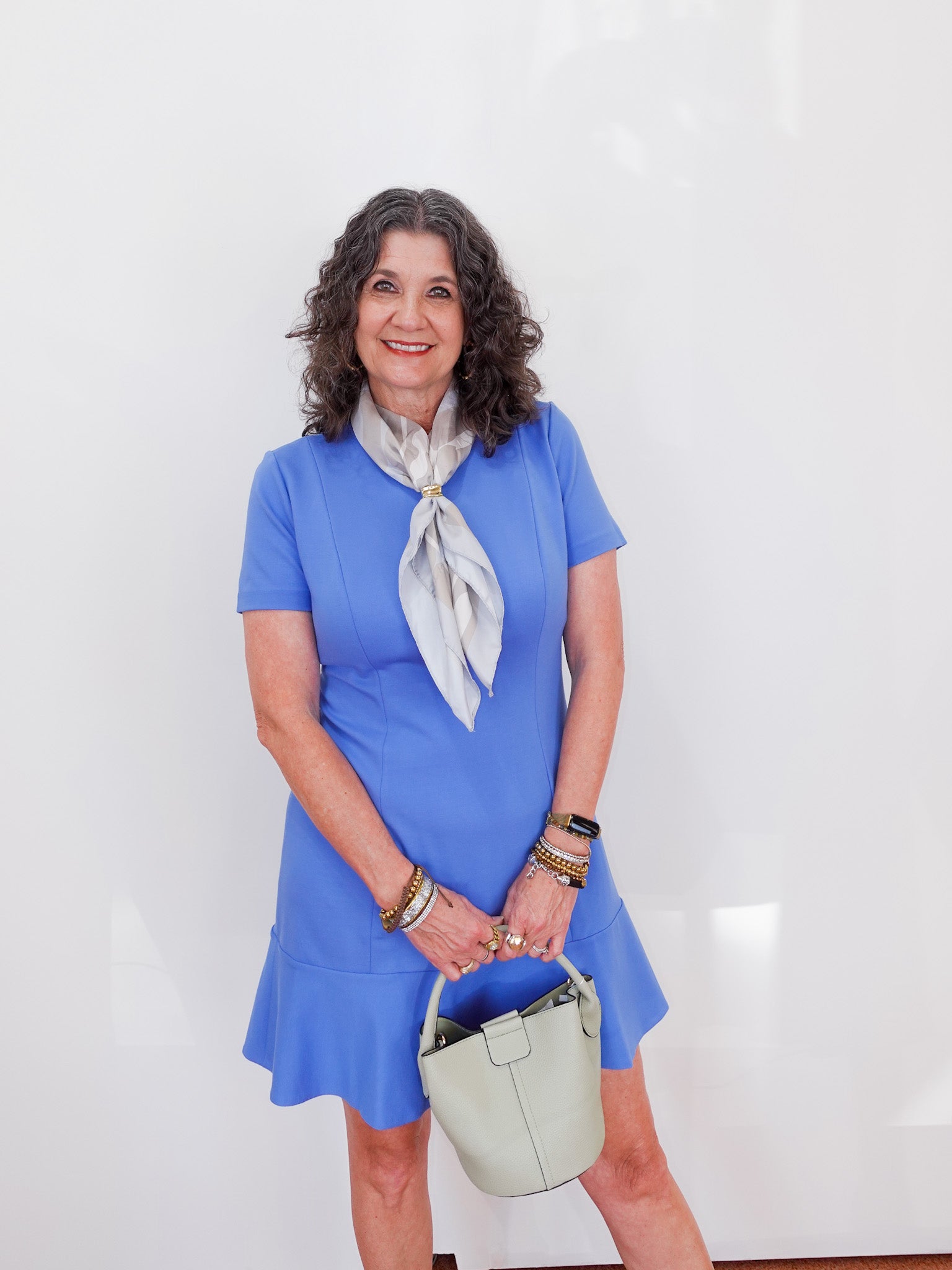 Woman in a blue dress with a white scarf and handbag against a white background