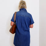Woman wearing a blue popover shirt dress with pockets in front a white background. 