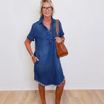 Woman wearing a blue denim dress standing against a white wall.