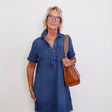 Woman wearing a blue popover shirt dress with pockets in front a white background. 